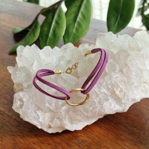Bracelet double en faux daim mauve, orné d’une breloque ovale plaquée flash or 18K, présenté sur fond neutre. Disponible en 15 coloris pour s’adapter à tous les styles.