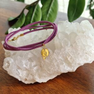 Bracelet triple tour en faux daim mauve, orné d’une pastille ronde et d’une feuille ajourée, toutes deux plaquées flash or 18K. Présenté sur fond clair. Disponible en 15 coloris.