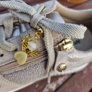 Breloque dorée en forme d’ange accompagnée d’une étoile, fixée sur une jolie basket. Le bijou est décliné en cinq couleurs éclatantes pour varier les styles.